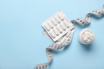 Bottle, blister packs with weight loss pills and measuring tape on blue background