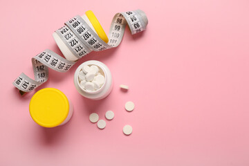 Bottles with weight loss pills and measuring tape on pink background