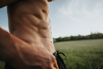 Close-up photo of a fit man displaying his toned abs while exercising outdoors at sunset. Fitness...