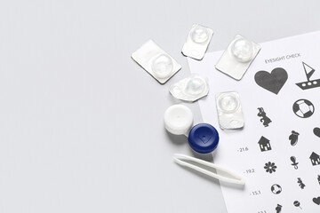 Eye test chart with tweezers, container and contact lenses on white background