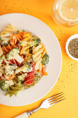 Delicious fusilli pasta with broccoli in plate, spices and glass of water on orange background
