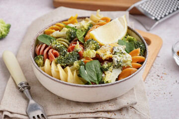 Delicious fusilli pasta with broccoli and lemon piece in bowl on light background, closeup