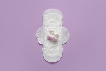 Menstrual pad and flowers on purple background