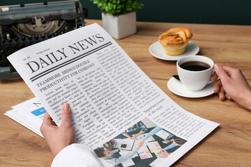 Female hands holding cup of coffee and newspapers on wooden table