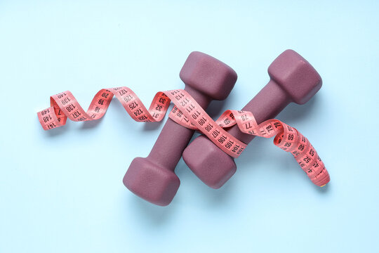 Dumbbells and measuring tape on color background