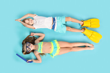 Cute little children with flippers and snorkeling mask lying on blue background