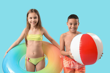 Cute little children in swimsuit with beach ball and inflatable ring on blue background