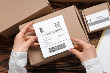 Woman sticking label to cardboard package on wooden table