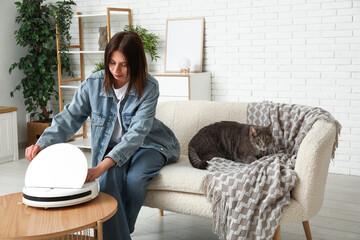 Young woman with robot vacuum cleaner and cute cat at home