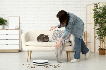 Emotional young woman, cute cat,  robot vacuum cleaner and scattered food at home
