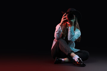 Stylish female photographer with modern camera taking picture of viewer on black background