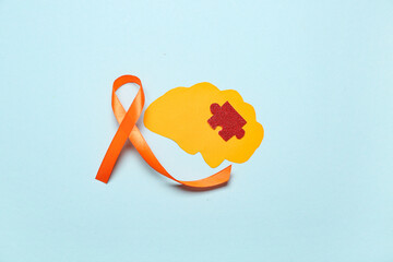 Paper brain with puzzle piece and orange ribbon on blue background. Multiple Sclerosis Awareness...