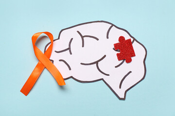 Paper brain, orange ribbon and puzzle on blue background. Multiple Sclerosis Awareness Month