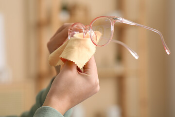 Beautiful young Asian woman wiping eyeglasses at home, closeup