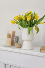 Beautiful vase of yellow tulips with candles and book in living room