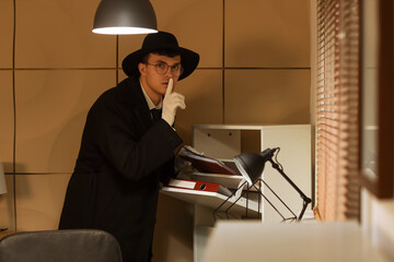 Male spy with folder showing silence gesture in office at night
