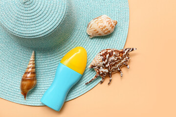 Bottle of sunscreen cream, seashells and hat on orange background
