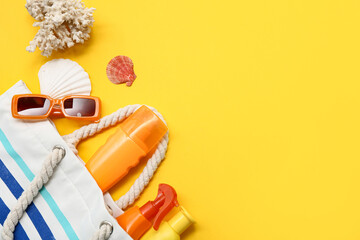 Bottles of sunscreen cream and beach accessories on yellow background