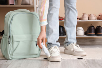 Woman in stylish sneakers with shoe polish and backpack at home