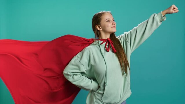 Portrait of jolly girl wearing superhero costume for Halloween, isolated over studio backdrop. Radiant teenage person dressed as comic book hero for event, showing courage and strength, camera B