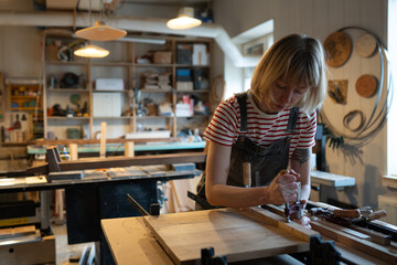 Concentrated female carpenter working on gluing wooden planks together, using clamping brackets and...