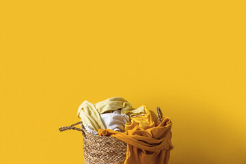 Basket with dirty clothes on yellow background