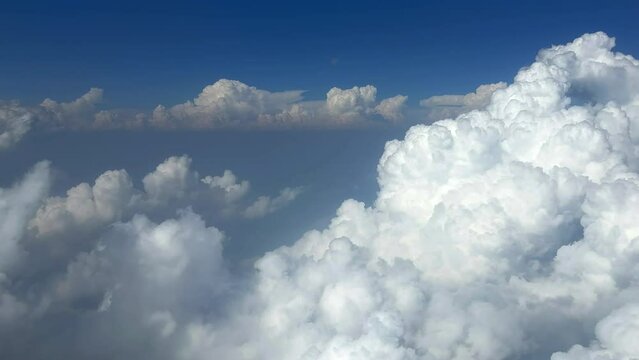 View of blue sky and white clouds from airplane window. Plane flying through clouds. Plane window view of blue sky with clouds moving past. 