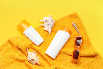 Composition with bottles of sunscreen cream, beach accessories and seashells on yellow background