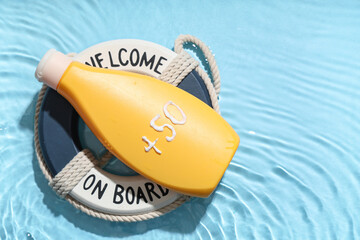 Bottle of sunscreen cream and decorative lifebuoy in water on color background