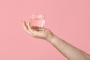 Male hand with glass of clean water on pink background