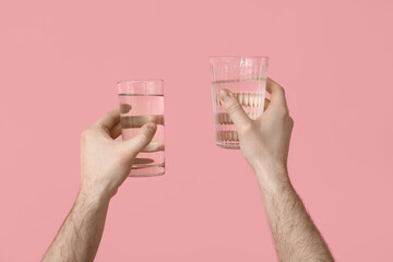 Male hands with glasses of clean water on pink background