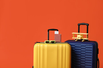 Suitcases with toy airplane, passport and eyeglasses on orange background. Travel concept