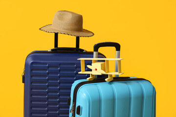 Blue suitcases with toy airplane and wicker hat on yellow background. Travel concept