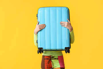 Young woman with blue suitcase on yellow background. Travel concept