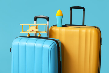 Suitcases with toy airplane and bottle of sunscreen cream on blue background. Travel concept