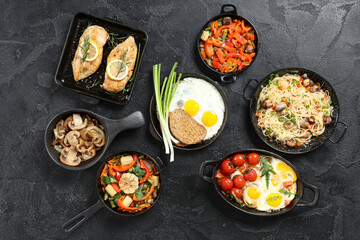 Frying pans with different dishes on dark background