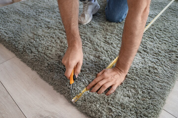 Young man with tape measure cutting carpet at home, closeup