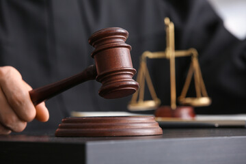 Male judge with gavel and scales of justice at table in courtroom