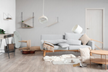 Blurred view of messy living room with sofa, shelves and tables