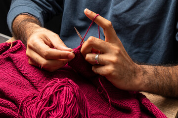 Manos de hombre tejiendo con palillos y lana