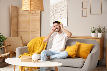 Young bearded man in headphones listening to music on sofa at home