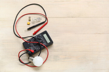 Multimeter, light bulb and electronics on wooden background