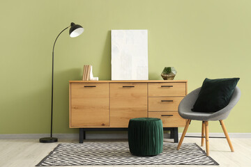 Chair, pouf, floor lamp and wooden chest of drawers near green wall in modern room