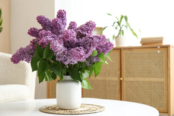 Vase with lilacs branches on coffee table in living room, closeup