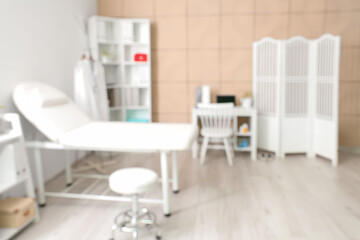 Blurred view of medical office with couch, folding screen and doctor's workplace