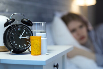 Sleeping pills with alarm clock on table of awake woman in bedroom at night, closeup