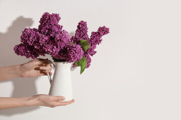 Female hands with blooming lilac flowers in jug on white background