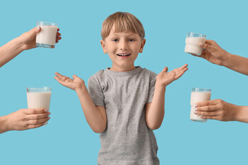 Cute little boy and hands with glasses of milk on blue background