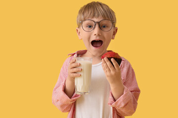 Surprised little boy with glass of milk and cupcake on yellow background