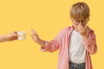Little boy covering nose and showing stop gesture against hand with glass of milk on yellow...